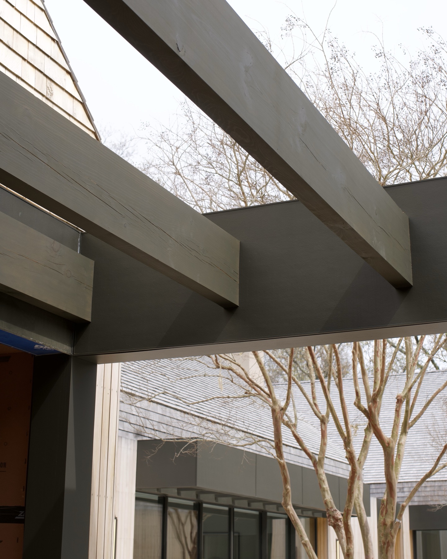 Covered walkway with dark timber pergola beams beside a shingled home